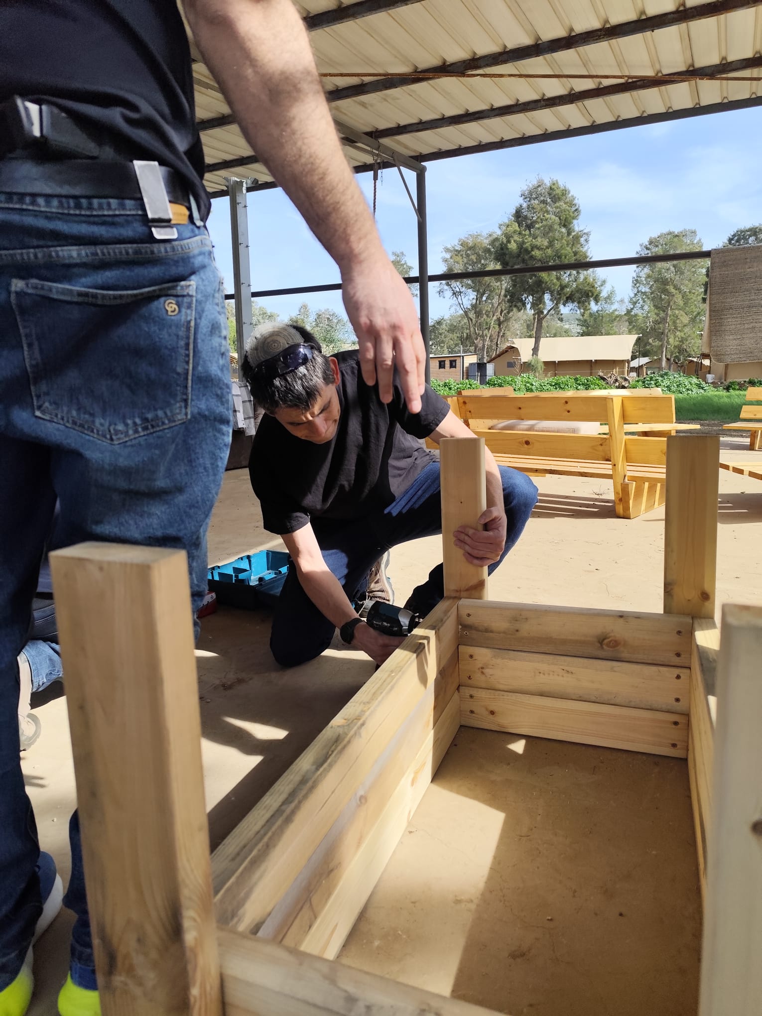 Participant assembling a wooden planter under the pergola